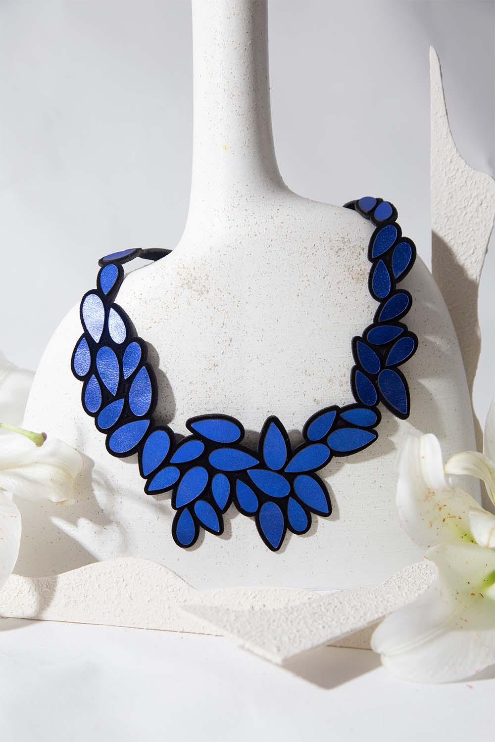Iskin Sisters Raindrop Blue floral necklace on a model on her back. Made of leather and suede with magnetic clasp. Handmade contemporary Jewelry.