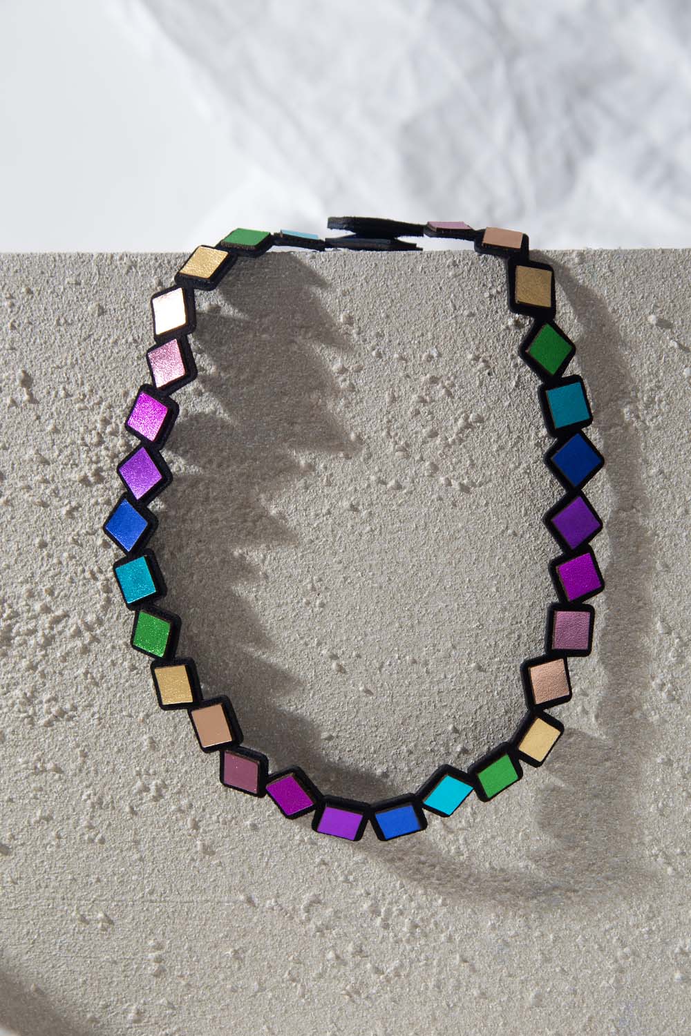 Necklace with colorful geometric squares on a textured surface. Lightweight. 
