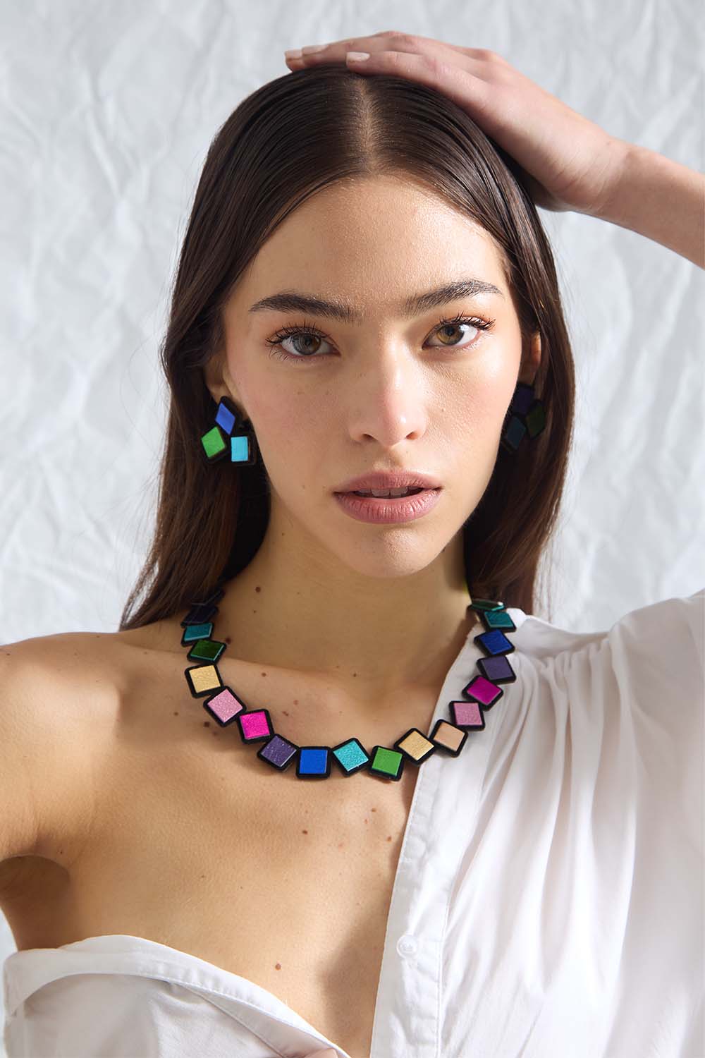 Woman wearing a colorful Iskin Sisters Rainbow necklace and earrings on a white background