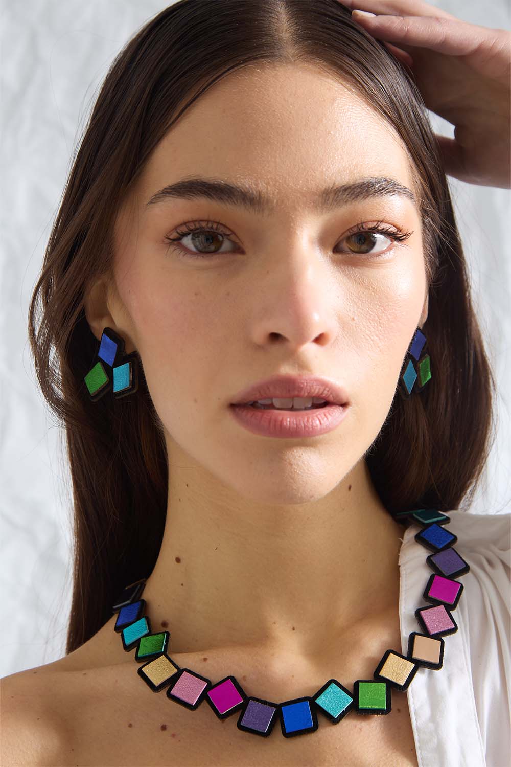 Woman wearing Iskin Sisters Rainbow colorful geometric necklace and earrings against a white background. Handmade contemporary jewelry. 