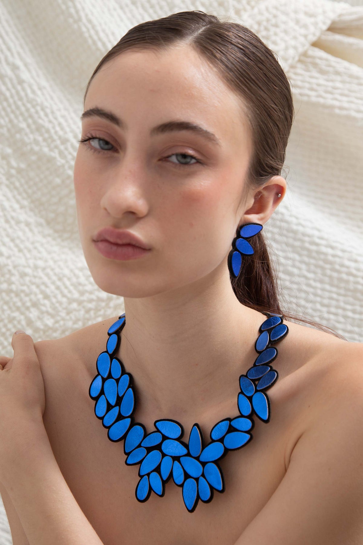 Woman wearing Iskin Sisters blue Raindrop leather earrings against a neutral background, handmade design