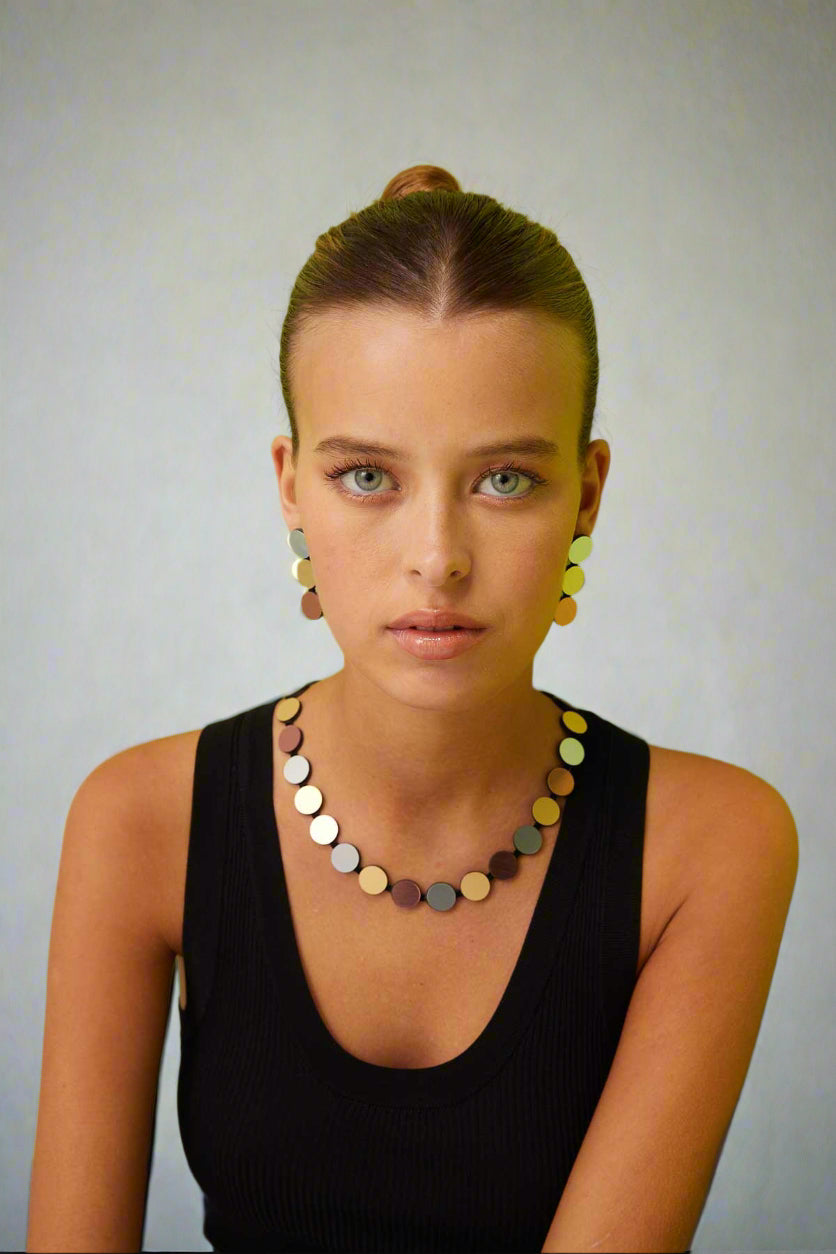 A woman wearing a black top and a geometric patterned necklace featuring silver, gold, and rose gold colors.